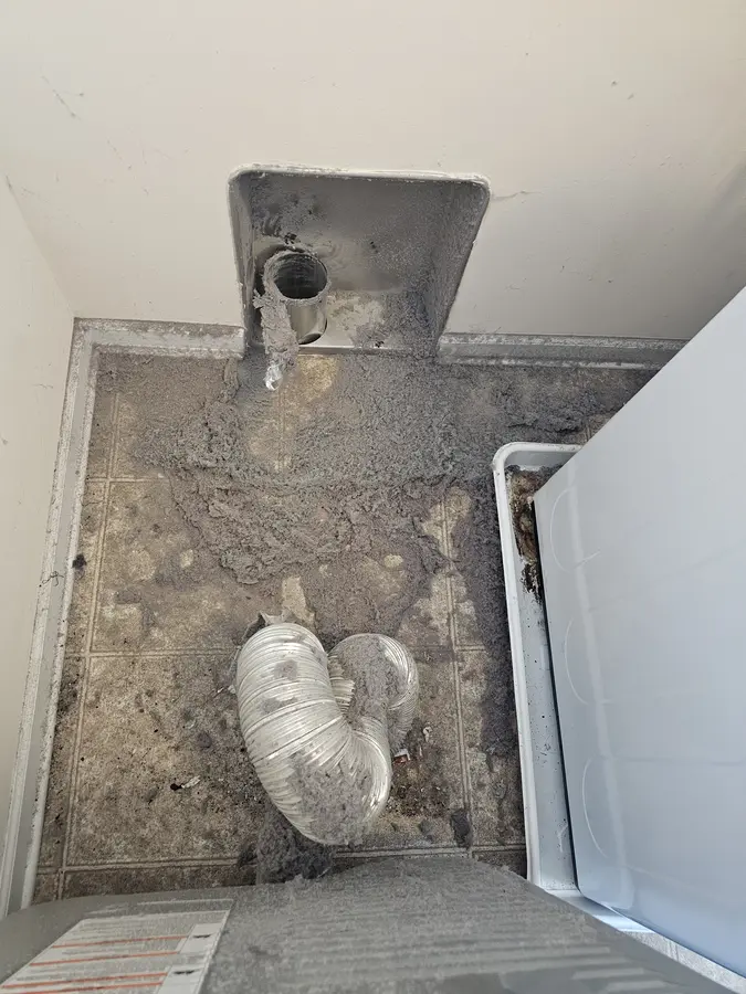 Before: Laundry closet floor covered in lint around a crushed foil duct