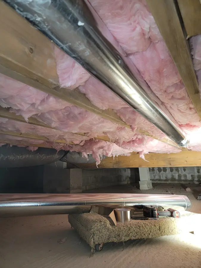 New smooth-wall metal dryer duct installed under floor joists in a crawlspace