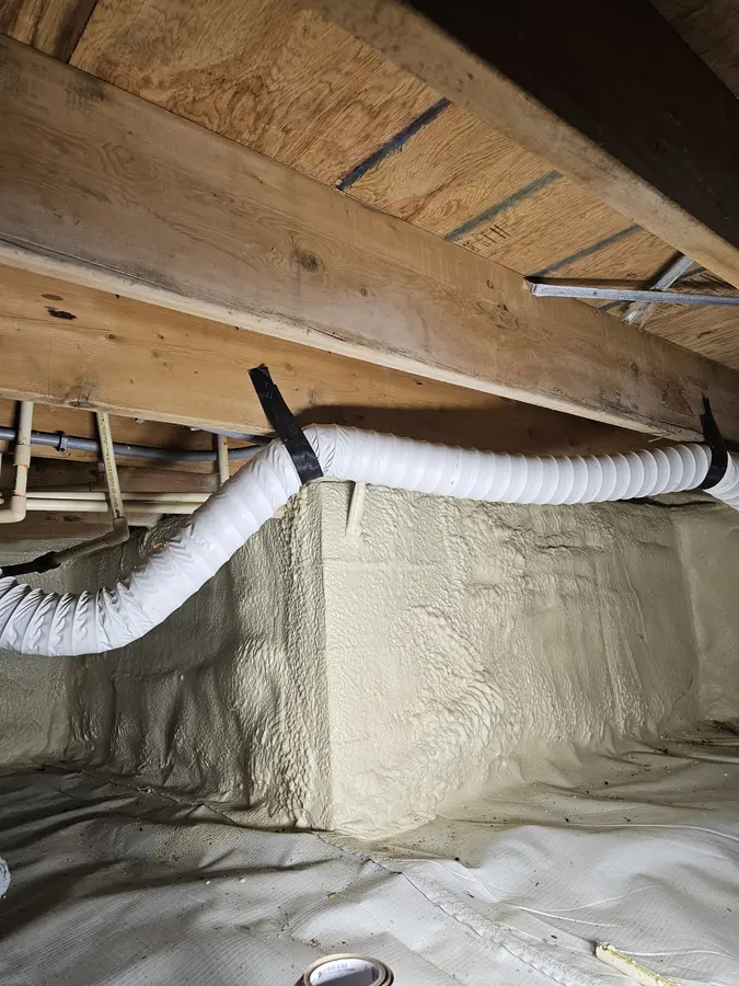 Before: White vinyl flex duct strapped under a floor